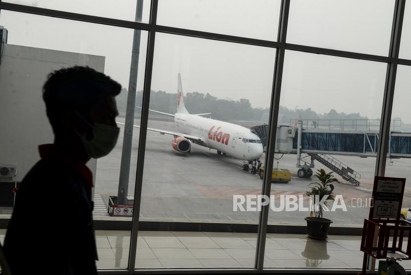 Penumpang melintas dengan latar belakang pesawat di Bandara Sultan Syarif Kasim II Pekanbaru, Riau, Sabtu (21/9).