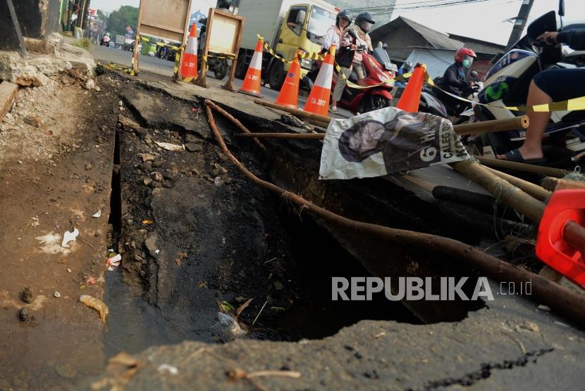 Pengendara motor melintas di dekat jalan yang amblas di Jalan Raya Sawangan, Depok, Jawa Barat, Jumat (28/6).