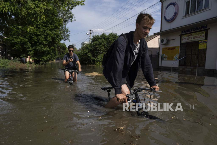 Penduduk setempat mengendarai sepeda mereka di sepanjang jalan yang banjir setelah bendungan Kakhovka meledak di Kherson, Ukraina, Selasa, (6/6/2023).