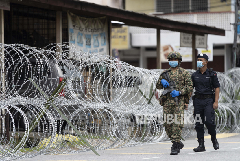 Personel tentara Malaysia dengan polisi berjaga didekat kawat berduri di area lockdown Selayang Baru, di luar Kuala Lumpur, Malaysia, Ahad (26/4). Lockdown tersebut dilakukan untuk memungkinkan aparat berwenang dalam melakukan penyaringan dan membantu mencegah penyebaran coronavirus