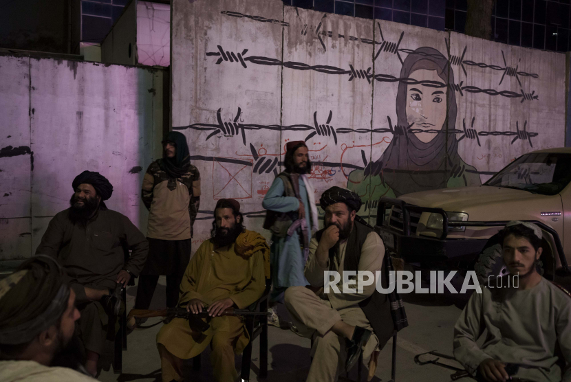 Anggota Taliban duduk di depan mural yang menggambarkan seorang wanita di balik kawat berduri di Kabul, Afghanistan, Selasa, 21 September 2021.