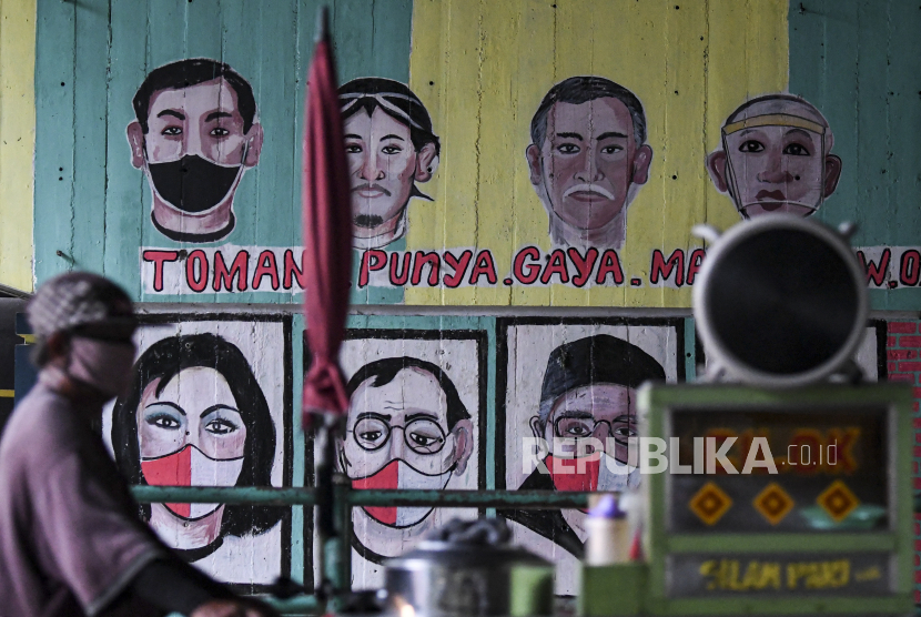 Pedagang yang mengenakan masker melintas di depan mural berisi pesan ajakan menggunakan masker.  (ilustrasi)