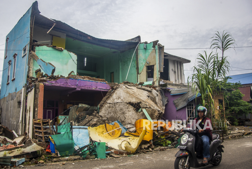  Seorang pria mengendarai sepeda motornya melewati sebuah rumah yang runtuh setelah gempa bumi di Mamuju, Sulawesi Barat, Indonesia, 17 Januari 2021. 
