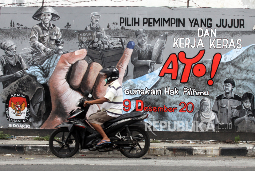 Pengendara melintas di depan mural bertema Pilkada serentak 2020 di kawasan Candi, Sidoarjo, Jawa Timur, Selasa (24/11/2020). Mural tersebut sebagai salah satu bentuk sosialisasi serta mendorong masyarakat untuk menggunakan hak suaranya dalam Pilkada serentak pada 9 Desember mendatang. 
