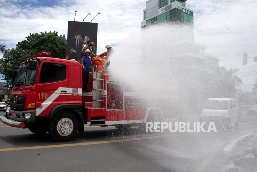 Petugas pemadam kebakaran menyemprotkan cairan disinfektan ke trotoar di Makassar, Sulawesi Selatan, Minggu (22/3/2020). 