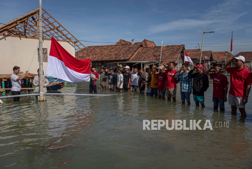 Warga membentangkan bendera merah putih di tengah banjir rob di Dusun Timbulsloko, Kabupaten Demak, Jawa Tengah. BNPB sebut adanya banjir di musim kemarau sudah menjadi fenomena global.