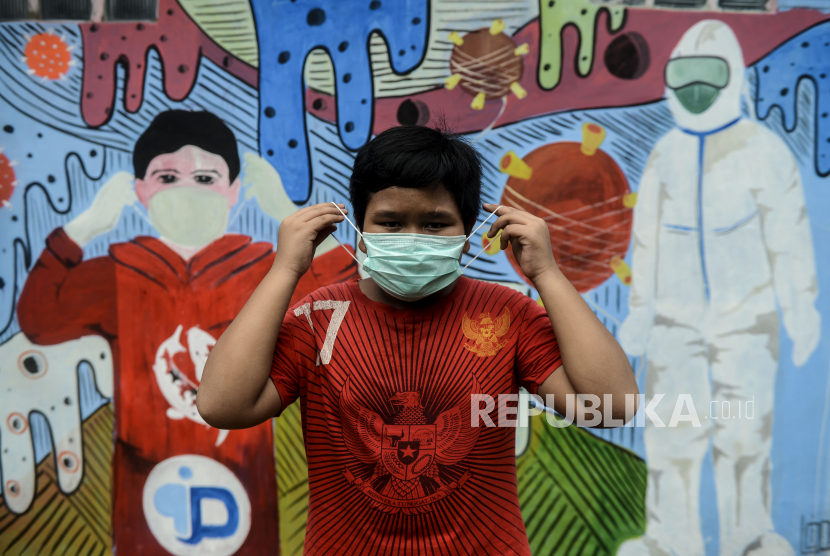 Seorang anak memakai masker di dekat tembok yang dihiasi mural saat pemberlakuan Pembatasan Sosial Berskala Besar (PSBB) di Depok, Jawa Barat, Rabu (15/4). Mural bertemakan virus Corona (Covid-19) itu menyosialisasikan kepada masyarakat untuk tetap di rumah. Per Rabu (15/4) pasien positif Covid-19 menembus angka 5.000 di Tanah Air.