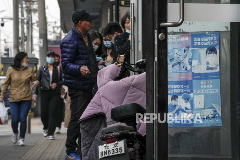 Orang-orang yang memakai masker wajah berkumpul di dekat pintu masuk toko yang memajang poster pudar yang mempromosikan vaksinasi COVID-19 di Beijing.