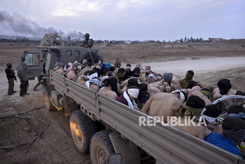 Tentara Israel berjaga di dekat truk yang berisi tahanan Palestina yang diikat dan ditutup matanya, di Gaza, Jumat, 8 Desember 2023.