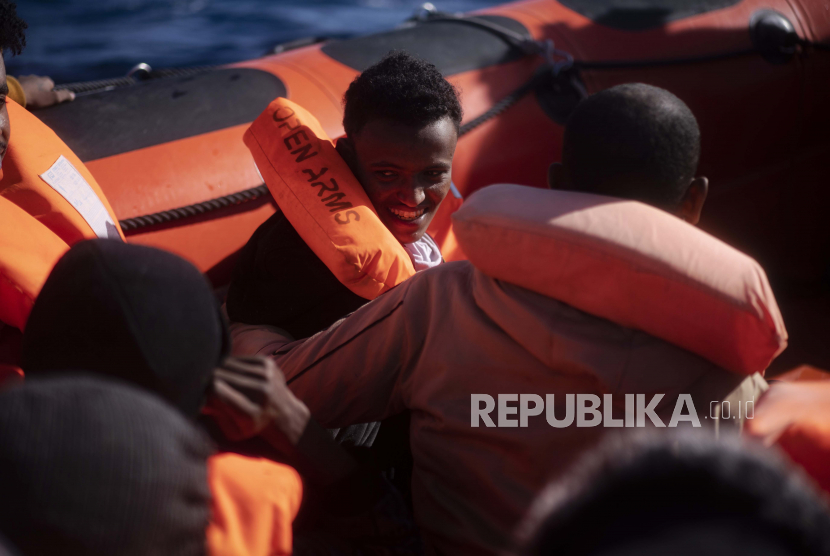Seorang migran tersenyum ketika dia dibantu oleh orang lain oleh pekerja bantuan dari LSM Spanyol Open Arms, setelah melarikan diri dari Libya dengan kapal kayu berbahaya di laut Mediterania, sekitar 110 mil utara Libya, pada Sabtu, 2 Januari 2021.