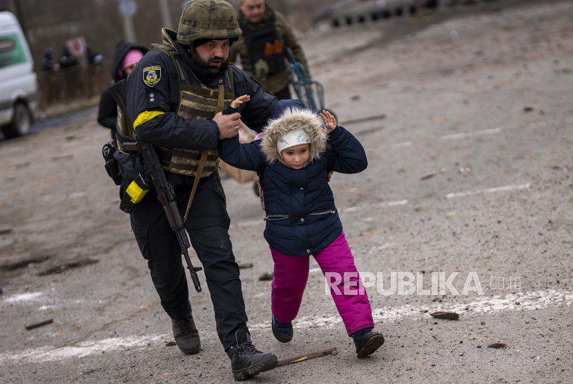 Seorang petugas polisi Ukraina berlari sambil menggendong seorang anak ketika artileri bergema di dekatnya, saat melarikan diri dari Irpin di pinggiran Kyiv, Ukraina, Senin, 7 Maret 2022. Terjebak di Basement Rumah Sakit, Anak Ukraina Rindukan Rumah
