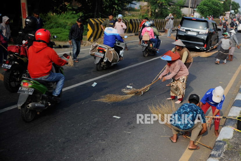 Sejumah warga menyapu koin yang dilemparkan pengguna kendaraan di jalur Jembatan Sewo, Kabupaten Indramayu, Jawa Barat, Rabu (19/4/2023). 