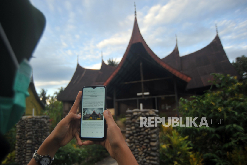 Pengunjung membaca sejarah dan informasi rumah gadang setelah scan kode QR di perkampungan adat Sijunjung, Sumatera Barat, Ahad (29/11/2020). Rumah gadang di kawasan itu dipasangi kode QR agar pengunjung dapat mengetahui sejarah dan informasi tentang masing-masing rumah sebagai upaya digitalisasi kampung adat .  