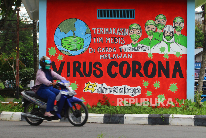 Seorang pengendara motor melintas di depan mural tentang pandemi COVID-19.