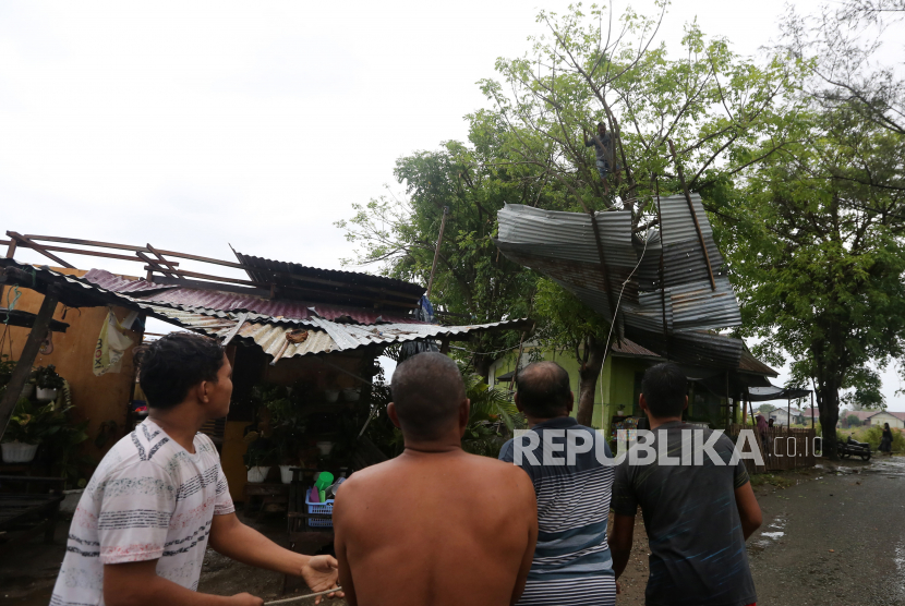 Sejumlah warga berupaya menurunkan atap rumah yang tersangkut di atas pohon akibat diterjang angin kencang (ilustrasi) 