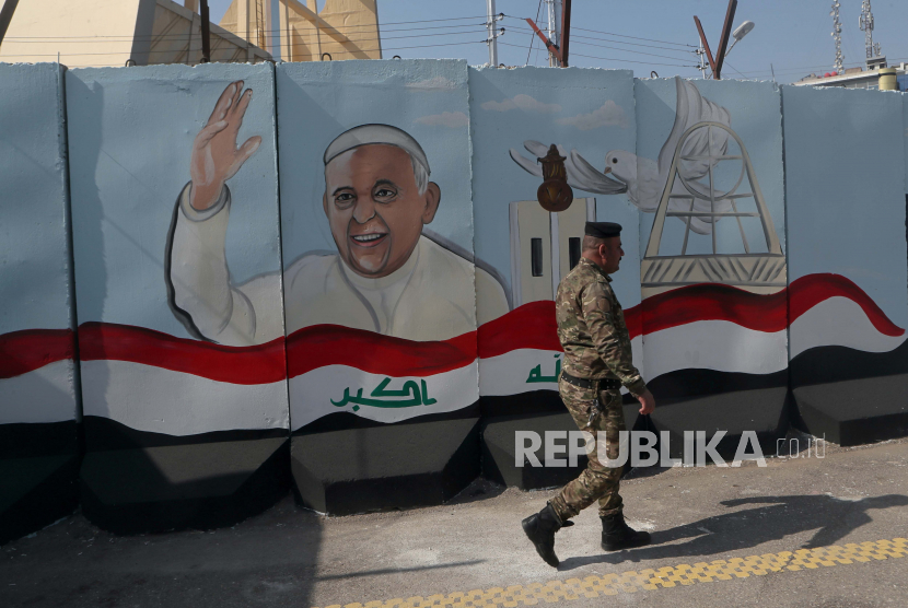 Seorang anggota angkatan bersenjata Irak berjalan melewati mural yang menggambarkan Paus Fransiskus, di dinding beton yang ditempatkan oleh pasukan keamanan Irak untuk mengelilingi Gereja Bunda Keselamatan selama persiapan kunjungan Paus, di Baghdad, Irak, Senin, 1 Maret 2021 .