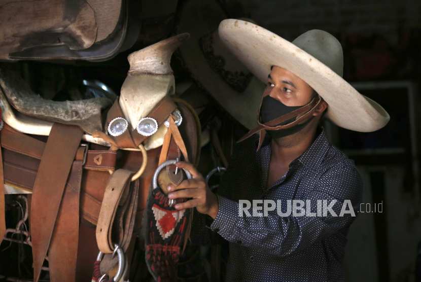 Koboi Meksiko atau Charro, Leonardo Flores memakai masker menumpuk pelana di arena berkuda Iztapalapa Charro, Mexico City, Senin (11/5). Flores datang ke arena setiap hari untuk memberi makan dan berolahraga kuda-kuda, terlepas dari pandemi virus corona  yang sedang berlangsung