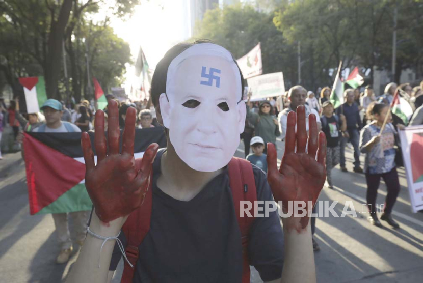 Seorang pria bertopeng wajah Benjamin Netanyahu dan tangan dicat merah melakukan pawai menentang perang terbaru Israel-Hamas dan mendukung Palestina di Gaza, di Mexico City, Minggu, 5 November 2023.