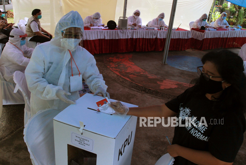 Petugas Kelompok Penyelenggara Pemungutan Suara (KPPS) berpakaian hazmat mengarahkan pemilih memasukan surat suara ke dalam kotak suara. (ilustasi)
