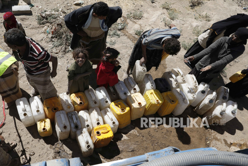  Anak-anak Yaman berdiri di samping kerabat mereka menunggu untuk mengisi jerigen dengan air dari tangki sumbangan di sebuah kamp Pengungsi Internal (IDP) di pinggiran Sana