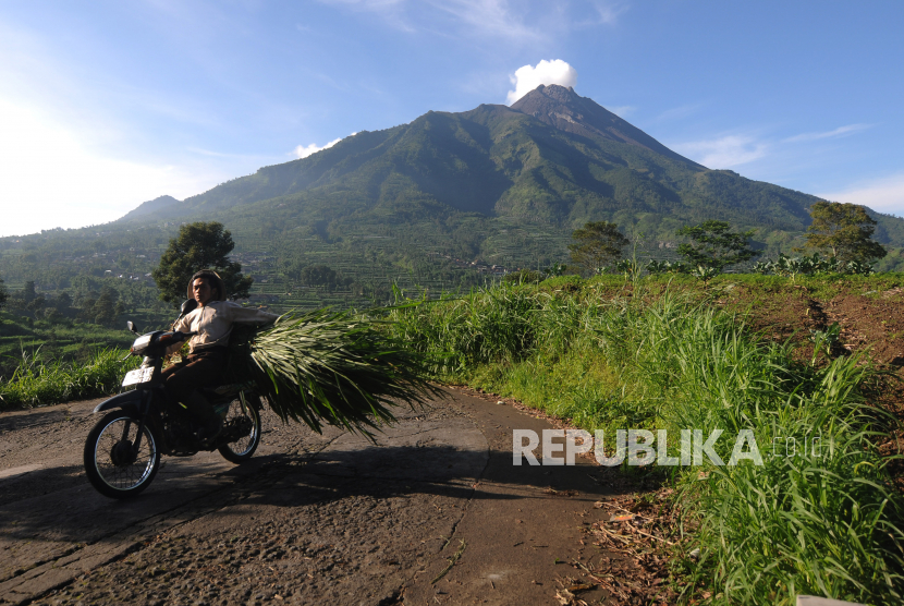 Warga melintas di jalan desa dengan berlatar belakang Gunung Merapi. 