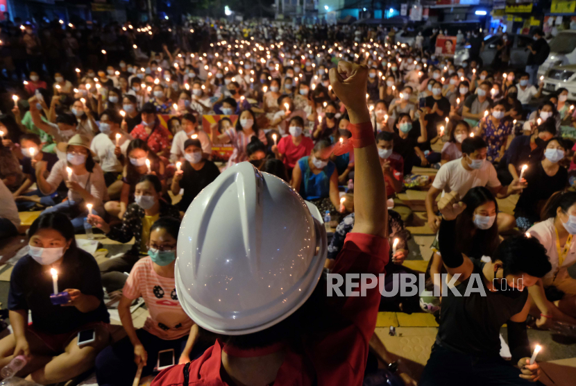 Seorang pengunjuk rasa anti-kudeta mengangkat tangannya dengan tangan terkepal di depan kerumunan selama demonstrasi malam dengan cahaya lilin di Yangon, Myanmar Minggu, 14 Maret 2021. Setidaknya empat orang ditembak mati selama protes di Myanmar pada hari Minggu, saat pasukan keamanan melanjutkan tindakan keras mereka terhadap perbedaan pendapat menyusul kudeta militer bulan lalu.