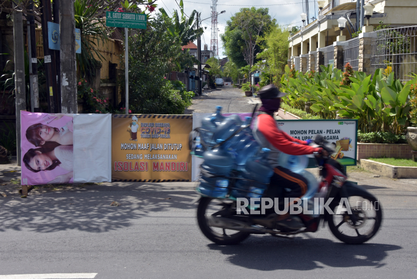 Seorang Pasien Covid-19 di Denpasar Sembuh. Pengendara motor melintas di dekat jalan perumahahan yang ditutup karena warganya melakukan isolasi mandiri di Denpasar, Bali.