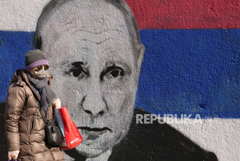 Seorang wanita melewati mural yang menggambarkan Presiden Rusia Vladimir Putin di Beograd, Serbia, Sabtu, 12 Maret 2022.