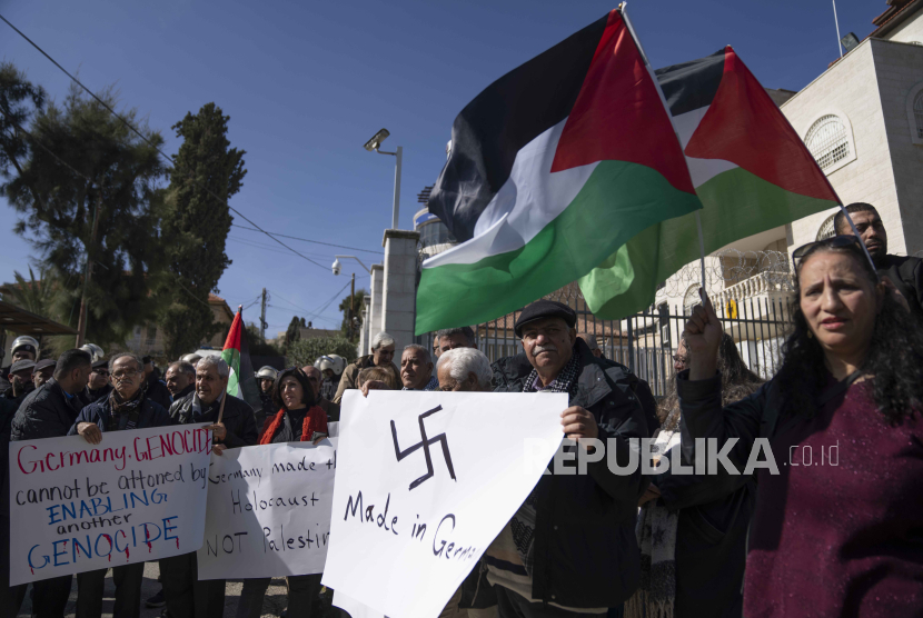 Palestinian activists carry posters and chant slogans while protesting against Germany