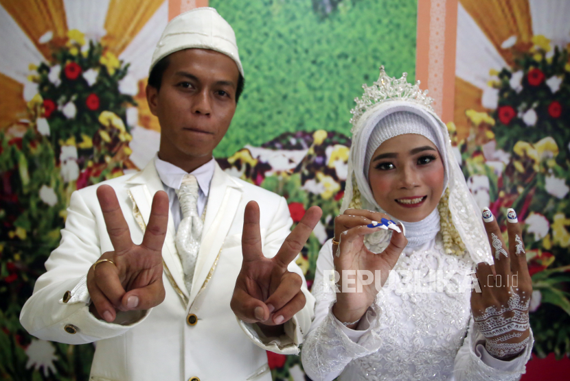 Sepasang pengantin menunjukan simbol 22022022 usai melangsungkan pernikahan di KUA Pamulang, Pamulang, Tangerang Selatan, Banten, Selasa (22/2/2022). Menikah di KUA, pengantin perempuan tetap harus terlihat cantik.