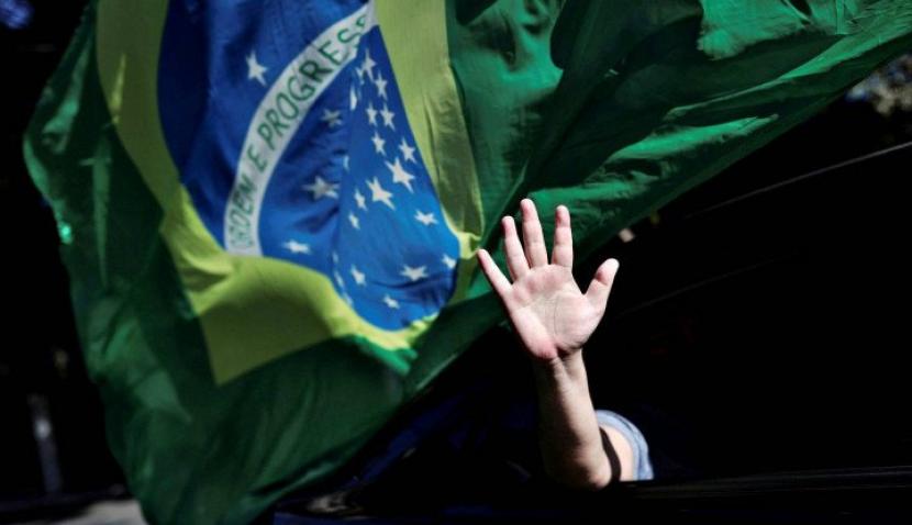 Seseorang melambai keluar dari jendela mobil saat pendukung Presiden Brazil Jair Bolsonaro melakukan protes atas tindakan karantina, di tengah penyebaran penyakit virus korona (COVID-19) di Sao Paulo, Brazil, Minggu (17/5/2020). (Reuters/Amanda Perobelli)