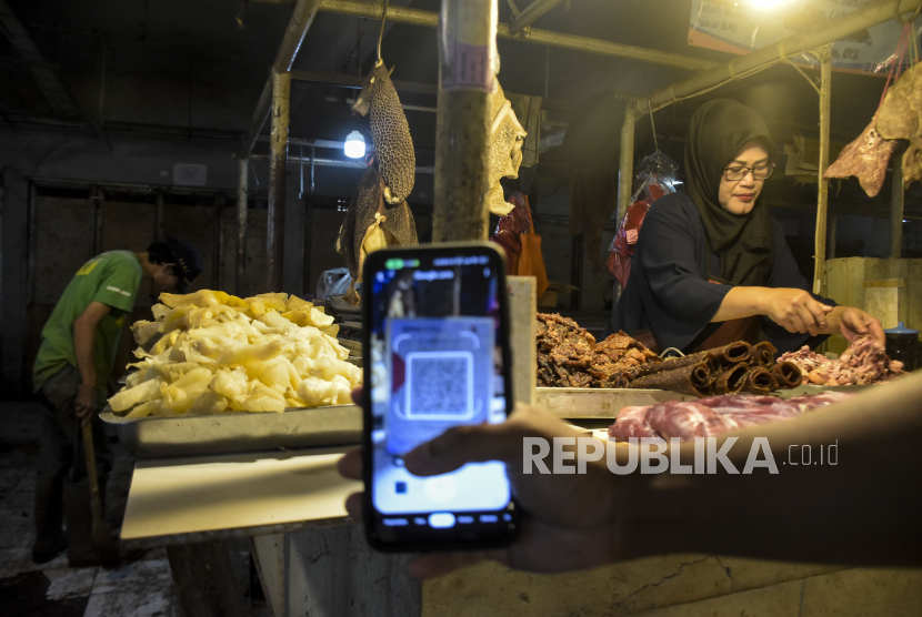 Warga melakukan transaksi digital menggunakan QRIS (Quick Response Code Indonesian Standard) saat membeli daging di Pasar Kosambi, Kota Bandung, Jawa Barat, Senin (10/7/2023). Bank Indonesia memberlakukan biaya layanan QRIS bagi Penyedia Jasa Pembayaran (PJP) sebesar 0,3 persen dari yang sebelumnya sebesar 0 persen atau gratis. Dalam aturan yang berlaku sejak 1 Juli tersebut, pedagang tidak boleh membebankan balik ke konsumen atau pembeli.