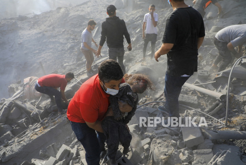 Seorang pria Palestina menggendong seorang anak yang meninggal saat yang lain mencari korban di antara puing-puing bangunan.