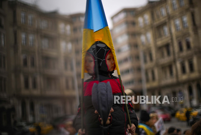 Seorang anak, sebagian tercermin dalam kaca, memegang bendera Ukraina selama protes oleh orang-orang pro-Ukraina terhadap invasi Rusia ke Ukraina, di Istanbul, Turki, Senin, 7 Maret 2022.