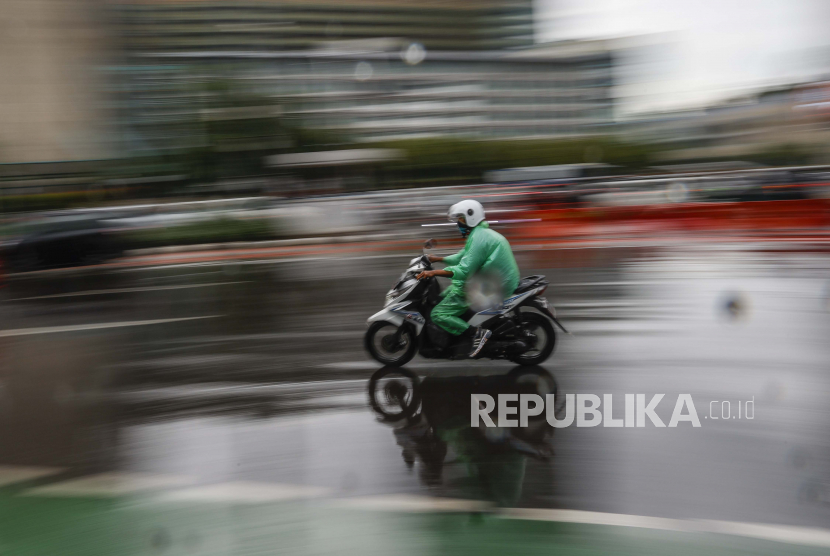 Gambar yang diambil dengan efek kecepatan rana lambat menunjukkan seorang pengendara sepeda motor yang mengenakan jas hujan, mengendarai sepeda motornya di jalan yang sibuk.