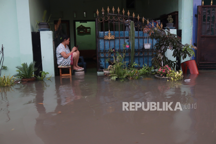 Warga berada di depan rumahnya yang tergenang banjir, (ilustrasi). 