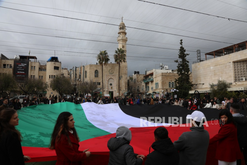 Umat Kristiani membentangkan bendera Palestina di depan Gereja Kelahiran di Bethlehem, Tepi Barat, Ahad (24/12/2023).