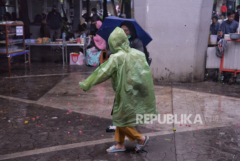 Warga mengenakan jas hujan untuk beraktivitas 
