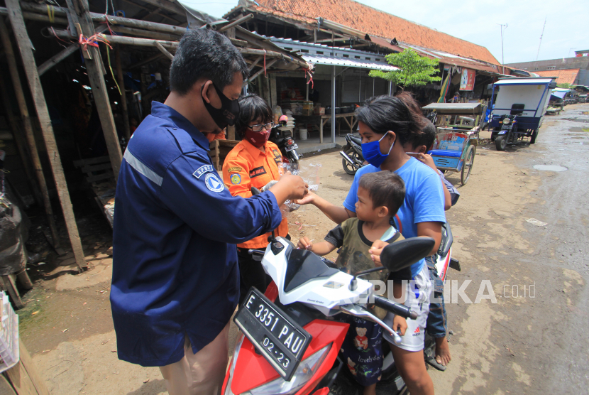Personel Badan Penanggulangan Bencana Daerah (BPBD) membagikan masker kepada warga di Pasar induk Indramayu, Jawa Barat, Jumat (18/12/2020). Pembagian masker tersebut dalam rangka sosialisasi penerapan protokol kesehatan untuk masyarakat di pasar tersebut guna menekan penyebaran COVID-19. 