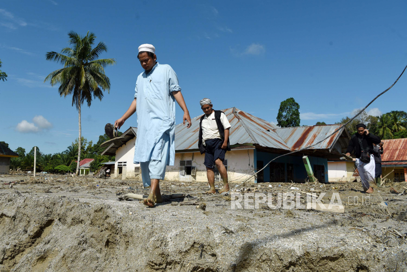 Warga melintas di dekat rumah yang tertimbun lumpur akibat banjir bandang di Desa Radda Masamba, kabupaten Luwu Utara, Sulawesi Selatan Selasa (21/07/2020). Tim SAR masih kesulitan membuka jalur trans Sulawesi akibat tingginya lumpur yang menutupi jalan. ANTARA FOTO/Yusran Uccang/hp.