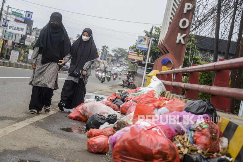 Warga berjalan di dekat sampah yang dibuang di pinggir jalan raya Kabupaten Bogor,