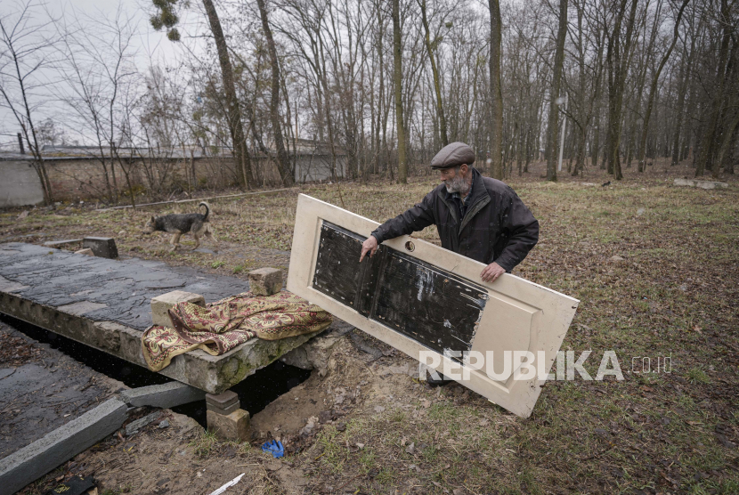 Seorang pria mengangkat pintu yang menutupi pembukaan kandang beton bawah tanah di mana mayat warga sipil yang dibunuh oleh pasukan Rusia, menurut penduduk, dibuang karena orang tidak dapat mengangkut mereka ke pemakaman di Bucha, Ukraina, Ahad, 3 April 2022 .
