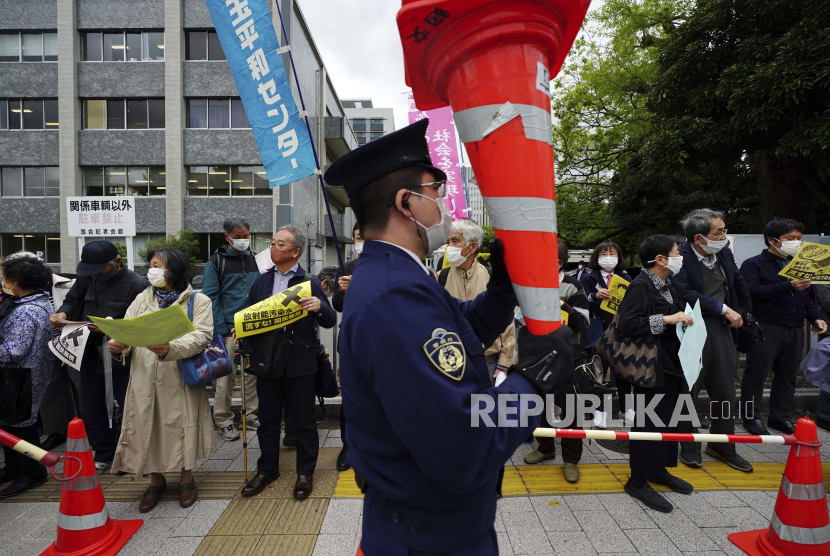 Seorang petugas polisi memegang kerucut lalu lintas saat orang-orang memprotes keputusan pemerintah untuk mulai melepaskan sejumlah besar air radioaktif yang diolah dari pembangkit nuklir Fukushima yang rusak ke laut, di luar kantor perdana menteri di Tokyo, Selasa, 13 April 2021. 
