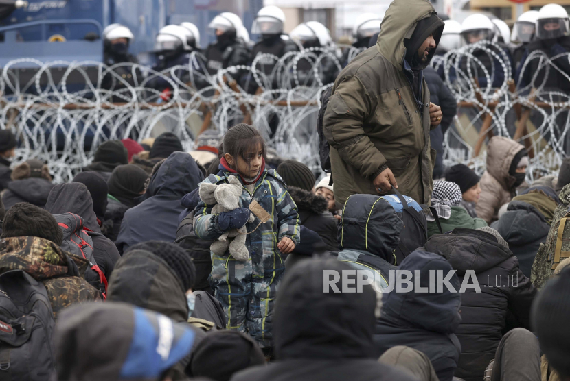  Para migran berkumpul di depan pagar kawat berduri dan tentara Polandia di pos pemeriksaan Kuznitsa di perbatasan Belarus-Polandia dekat Grodno, Belarus, pada Senin, 15 November 2021.