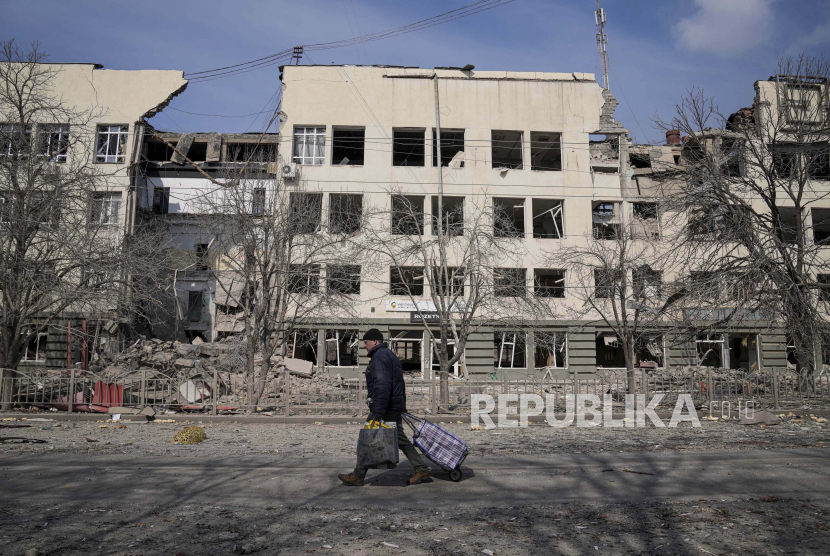 Seorang pria berjalan melewati sebuah bangunan yang rusak akibat penembakan di Mira Avenue (Avenue of Peace) di Mariupol, Ukraina, Ahad 13 Maret 2022. Pasar saham dunia pulih pada Rabu (16/3/2022) karena pasar mengamati tanda-tanda harapan dalam konflik Ukraina.