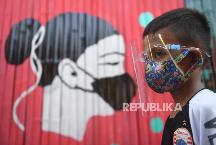 Seorang anak melintasi mural bertema Covid-19 di Jakarta.