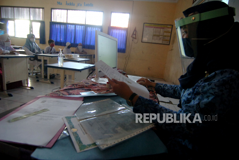 Seorang guru yang mengenakan pelindung wajah dan masker membantu siswa dan wali murid melakukan pendaftaran Penerimaan Peserta Didik Baru (PPDB) secara daring. Ilustrasi