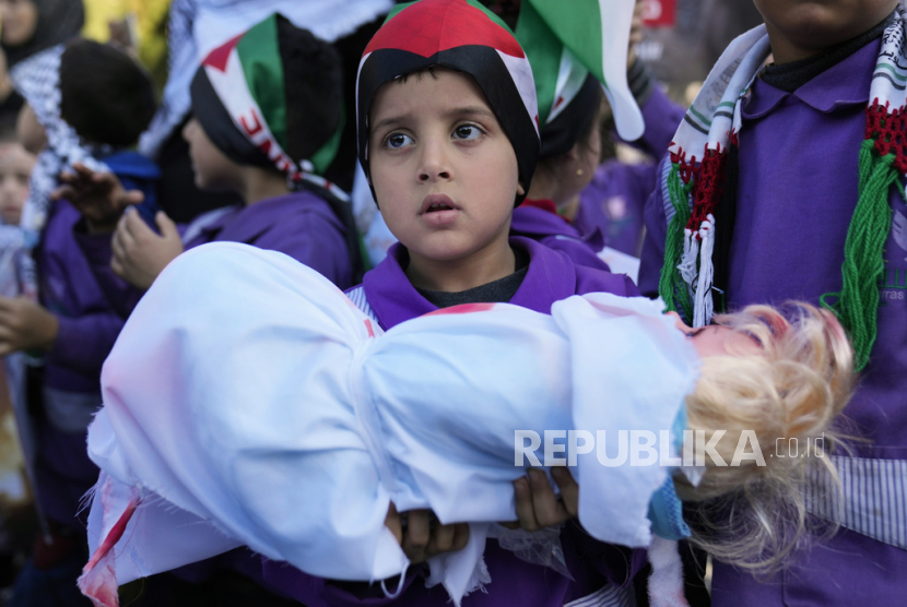 Seorang siswa sekolah dasar Palestina menggendong jenazah anak-anak Palestina tiruan, saat ia menghadiri aksi duduk bersama siswa lainnya di luar kantor Delegasi Uni Eropa untuk Lebanon, untuk menunjukkan solidaritas mereka terhadap rakyat Palestina di Gaza, di Beirut, Lebanon, Kamis, (14/12/2023).