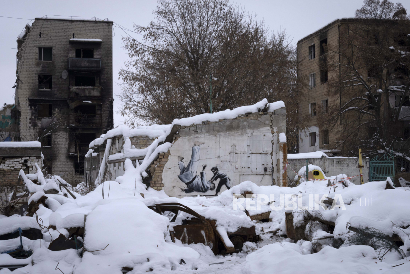 Sebuah karya seni yang dibuat oleh seniman jalanan Inggris Banksy di sebuah bangunan yang dihancurkan oleh tentara Rusia, terlihat di antara puing-puing yang tertutup salju di Borodyanka, wilayah Kyiv, Ukraina, Selasa, 6 Desember 2022.