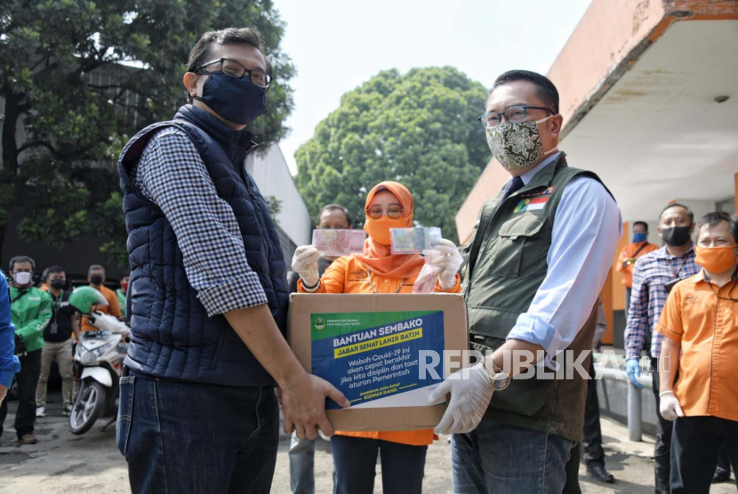 Gubernur Jawa Barat Ridwan Kamil (kanan) secara simbolis menyerahkan bantuan sembako saat melepas petugas pos dan ojek online (ojol) untuk menyalurkan bansos kepada Keluarga Rumah Tangga Sasaran (KRTS) di Kantor Sentral Pengolahan Pos (SPP) Bandung, Kota Bandung, Ahad (19/4). Bantuan sosial (bansos) senilai Rp 500 ribu dari Pemda Provinsi Jabar merupakan bantuan kepada warga terdampak pandemi COVID-19